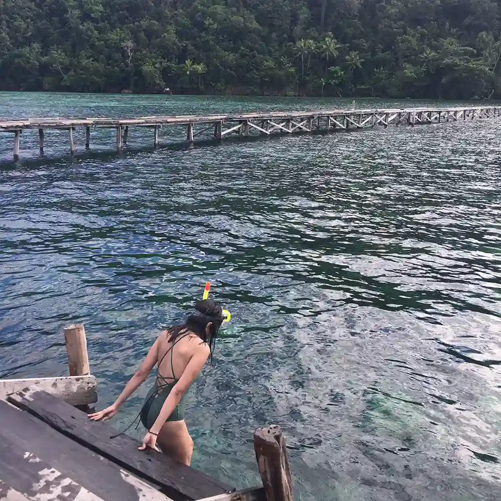 A snorkeller entering the water from a timber jetty in flat morning conditions