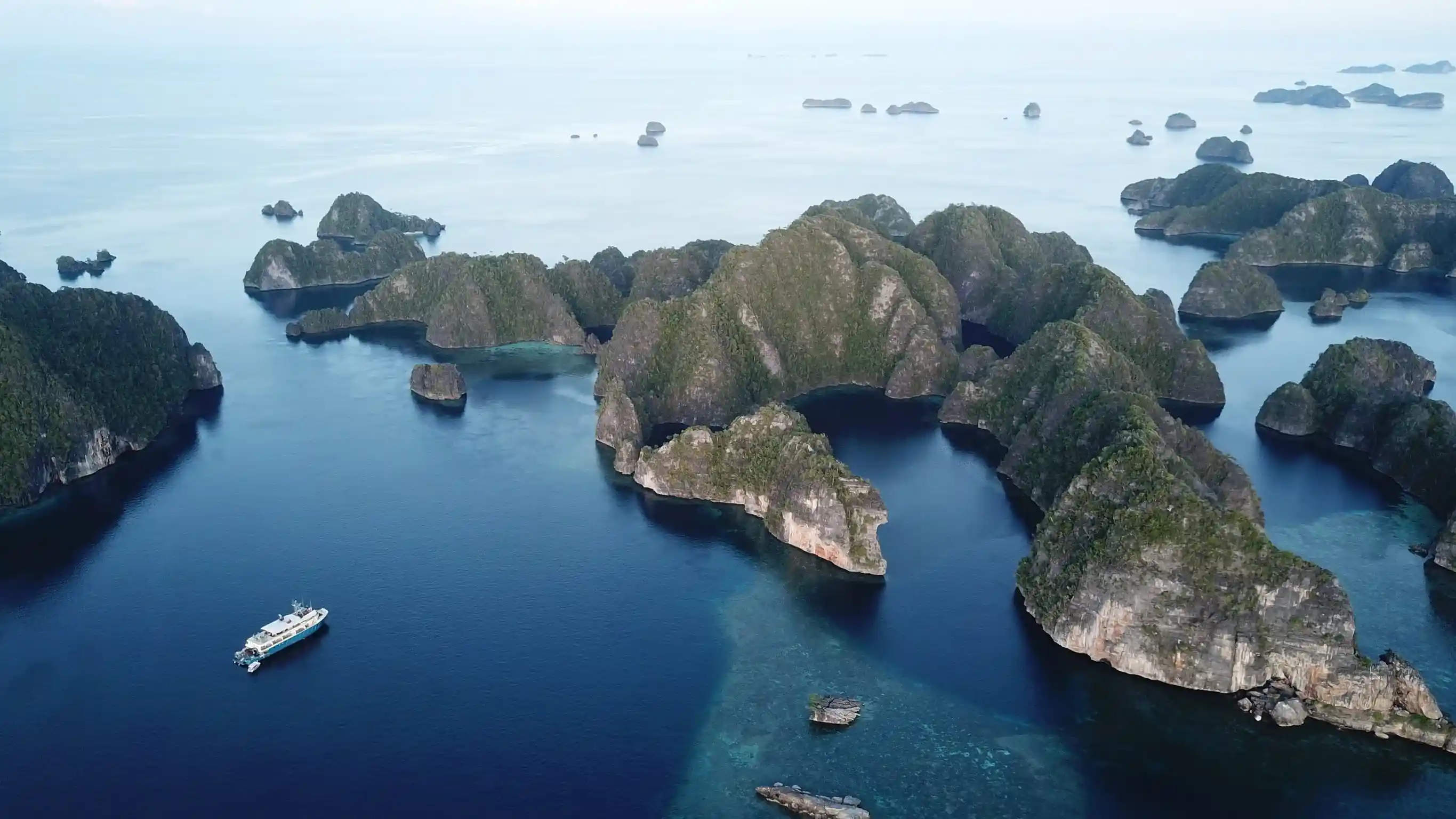 An exploration yacht threading a maze of forested limestone islets, seen from the air