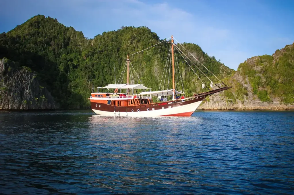Akomo Isseki phinisi anchored beneath forested limestone cliffs